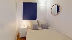 Un dormitorio con una cama, una mesita de noche, un espejo en la pared y una ventana con persiana azul.