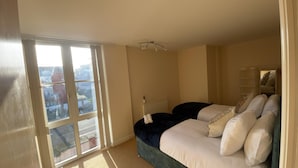 Camera da letto con un'ampia porta-finestra in vetro, un letto con molti cuscini, un termosifone e un lampadario.