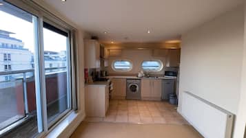 A compact kitchen with a washing machine, a microwave, and a sink. There are two windows providing natural light.