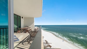 Uma varanda com vista para o mar, uma mesa e cadeiras.
