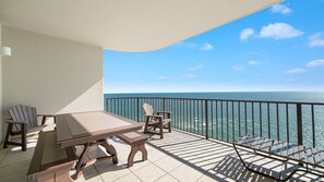 Een balkon met uitzicht op de oceaan, een tafel, stoelen en een ligbed.