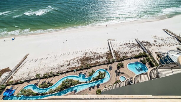 Vista aérea de um resort à beira-mar, com área de piscina, praia de areia e oceano cristalino.