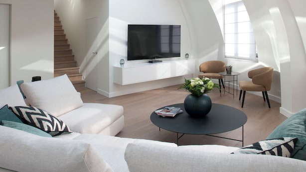 A modern living room with a large TV, comfortable seating, and a unique skylight design. - Chic penthouse Grand-Place  (Brussels)