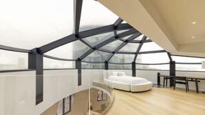 A modern loft bedroom with a curved glass ceiling, a white bed, and a dining area. - Chic penthouse Grand-Place  (Brussels)