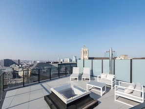 A rooftop terrace with a glass balustrade, white lounge chairs, a glass-top table, and a view of the city skyline. - Chic penthouse Grand-Place  (Brussels)