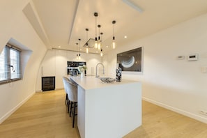 A modern kitchen with a central island, pendant lighting, and a view of the dining area. - Chic penthouse Grand-Place  (Brussels)