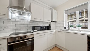 Une cuisine moderne avec des meubles blancs, une hotte en acier inoxydable, un four à micro-ondes et un four encastré.