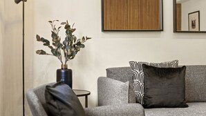 Un salon moderne avec un canapé gris, des coussins à motifs noir et blanc, un lampadaire et un vase contenant des feuilles vertes.