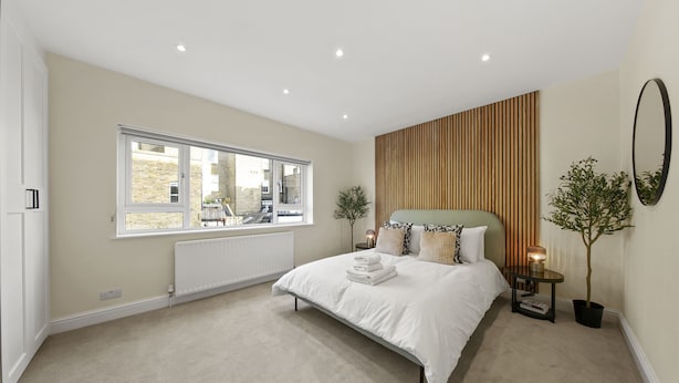 Une chambre à coucher avec un grand lit, une fenêtre, un radiateur, une table de chevet avec une lampe et une plante en pot.