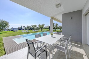 A covered outdoor area with a pool, white table, and chairs. - Villa Easy chic in Moniga del Garda with private pool (Moniga del Garda)