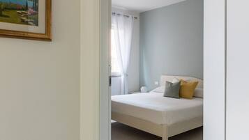 A bedroom with a bed, a window with curtains, and a painting on the wall.