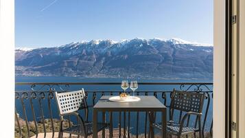 A balcony with a table and chairs overlooking a mountainous landscape and a body of water.