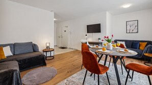 Una sala de estar moderna con comedor, que incluye un sofá, una mesa de centro y un televisor montado en la pared.