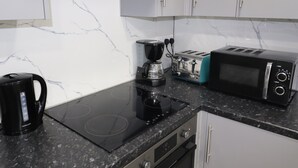 A modern kitchen with a black induction cooktop, a coffee maker, a toaster, and a microwave. - Impeccable 1-bed Apartment in Dartford (Dartford)