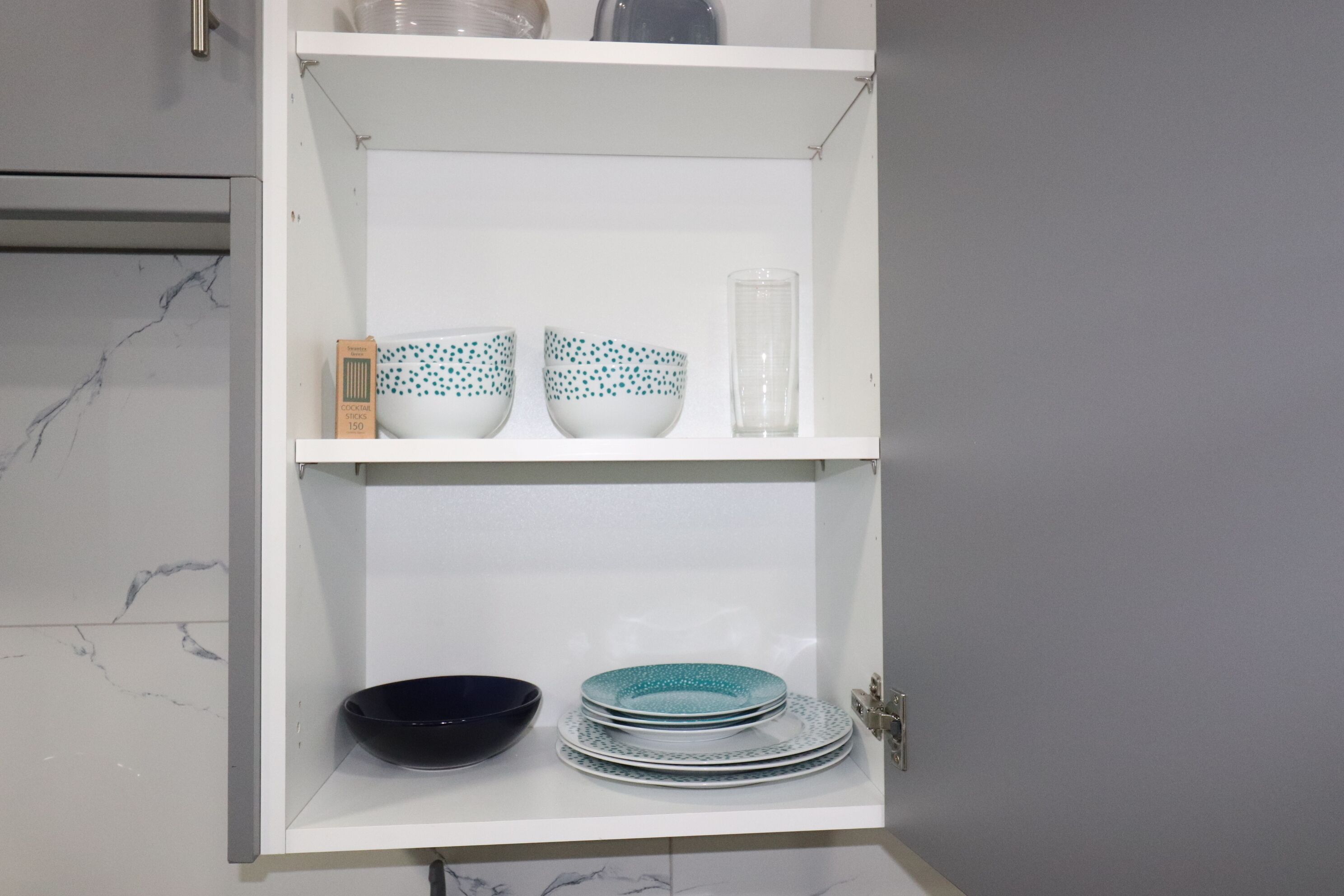 A white cabinet with shelves holding various bowls and plates.