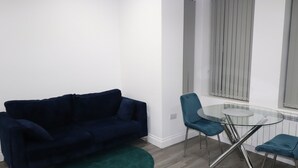A modern living room with a dark blue sofa, a glass coffee table, and teal chairs. - Impeccable 1-bed Apartment in Dartford (Dartford)