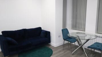 A modern living room with a dark blue sofa, a glass coffee table, and teal chairs.