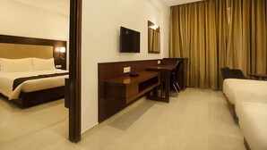 A hotel room with two beds, a desk, a TV, and a large window with curtains. - HOTEL AADRIKA (Chikkamagaluru)
