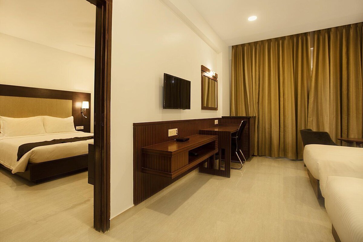 A hotel room with two beds, a desk, a TV, and a large window with curtains.