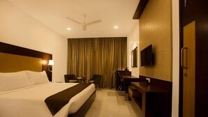 A hotel room with a large bed, a desk, a chair, a television, and a curtain. - HOTEL AADRIKA (Chikkamagaluru)