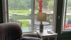 Et værelse med en brun lædersofa, et lille bord med en lampe og store vinduer med udsigt over en have.