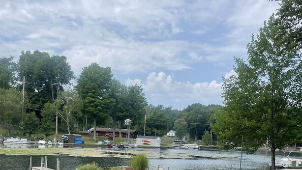 Udsigt over en sø med græsareal, picnicbord og en dok med både.