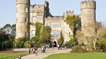 A historic castle with multiple towers, a central entrance, and a surrounding garden.
