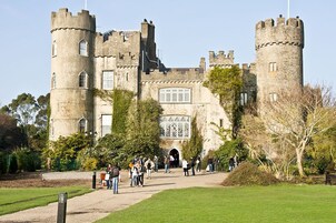 Un castillo histórico con múltiples torres, una entrada principal y un jardín circundante.