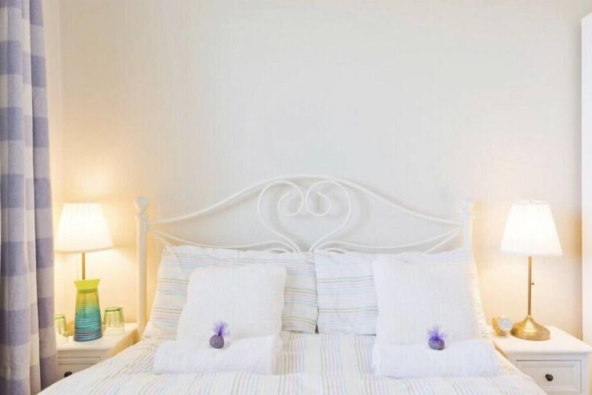 Una cama bien tendida con sábanas blancas y dos almohadones decorativos, flanqueada por mesitas de noche con lámparas.