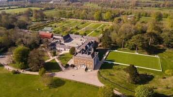 Vista aérea de una extensa propiedad con un edificio destacado, amplios jardines verdes y un jardín bien cuidado.