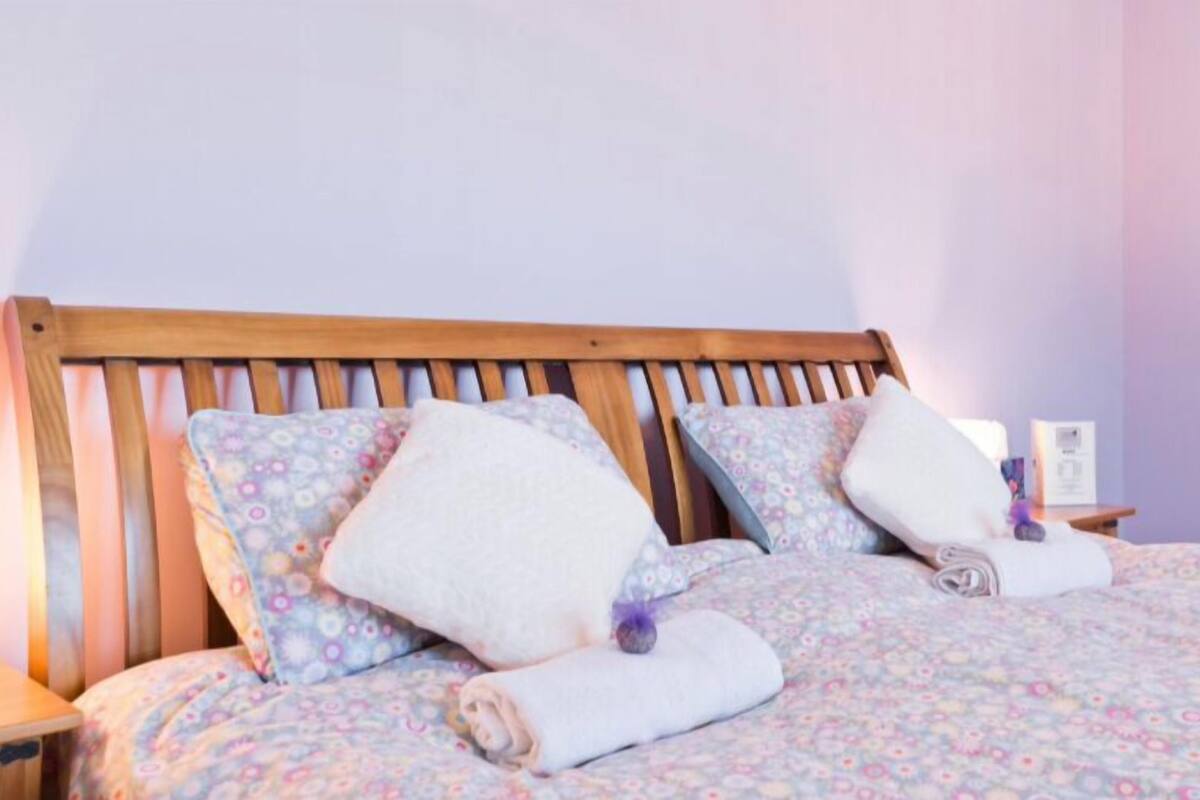 Una cama con ropa de cama floral, dos almohadas y un cabecero de madera.