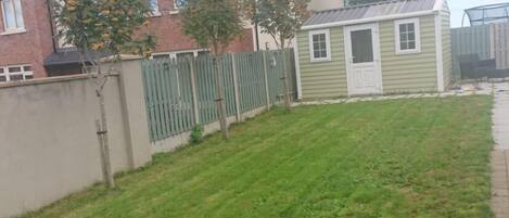 A residential area with a well-maintained lawn, a small shed, and a brick house with a sloped roof.