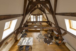 A high-ceilinged room with exposed wooden beams, a chandelier, a dining table set, and a leather sofa. - City penthouse Grand-Place (Brussels)