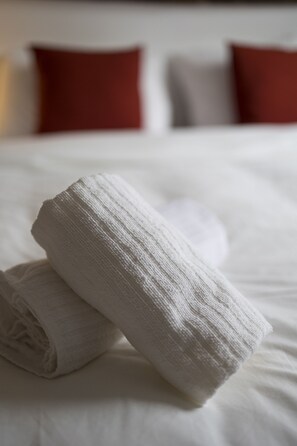 Una cama bien hecha con una toalla blanca enrollada y dos almohadas al fondo.