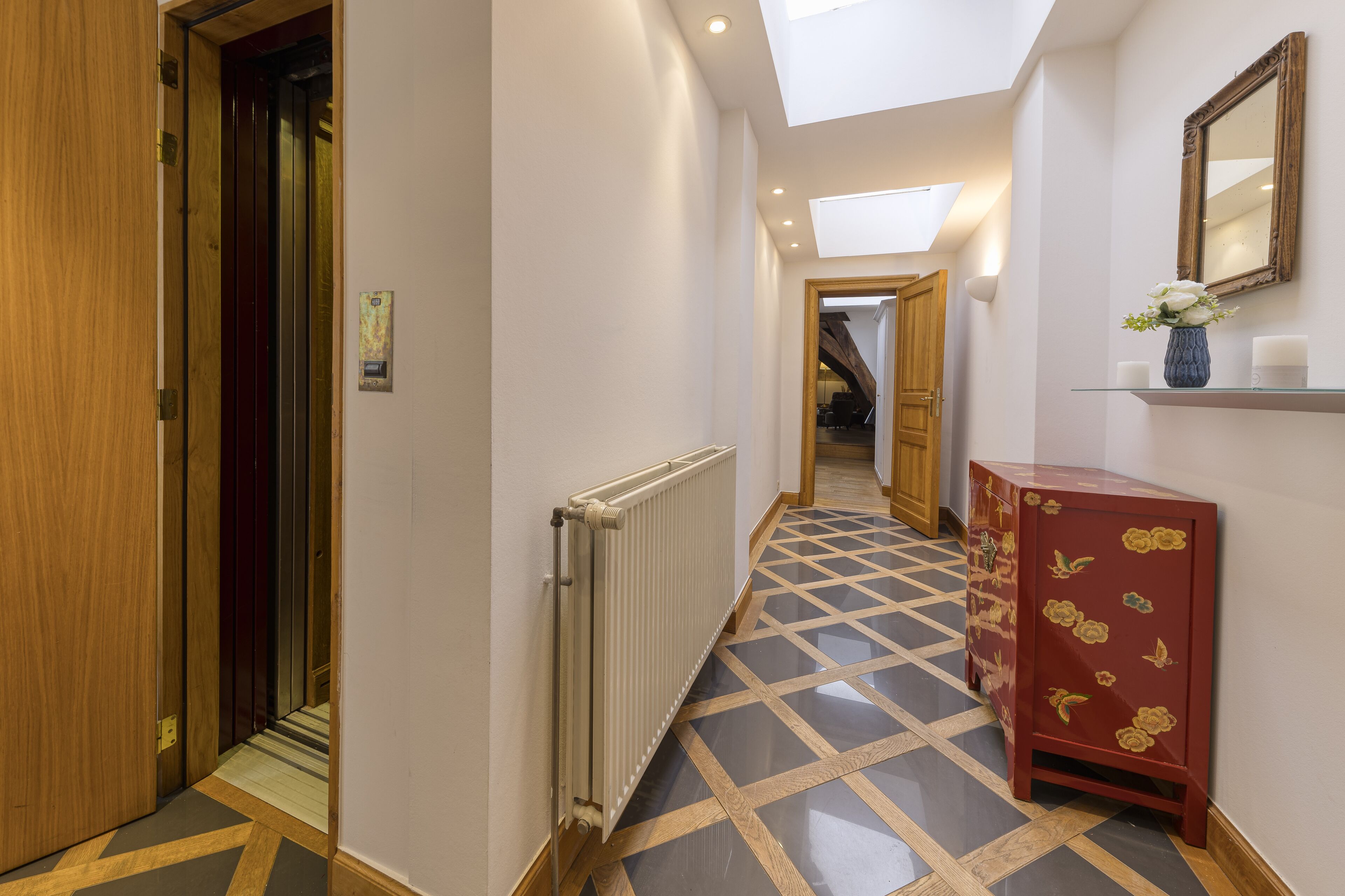 A hotel hallway with a radiator, wooden door, and a red cabinet with floral designs.