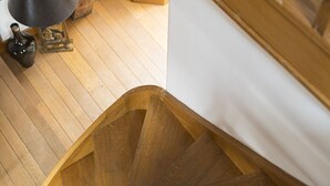 Een houten trap met een witte muur en een zwarte vaas op de vloer.