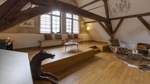Een ruime loft met houten balken, een groot raam, een open haard en een beeld van een paard.