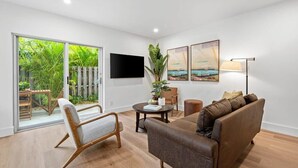 A modern living room with a sofa, armchair, and a flat-screen TV mounted on the wall. - Fresh & Bright Condo 1BR/1BA – Near Riverwalk (Fort Lauderdale)