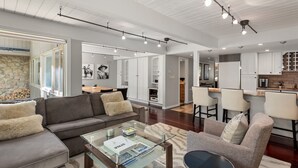 A modern living room with a sofa, armchairs, a glass coffee table, and a kitchen area with white cabinets and a brick accent wall. - Aspen Alps Apartment #107 2 Bedroom Condo by RedAwning (Aspen)