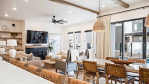 Uma sala de estar moderna com uma TV grande, assentos confortáveis, uma área de jantar e vista para o exterior.