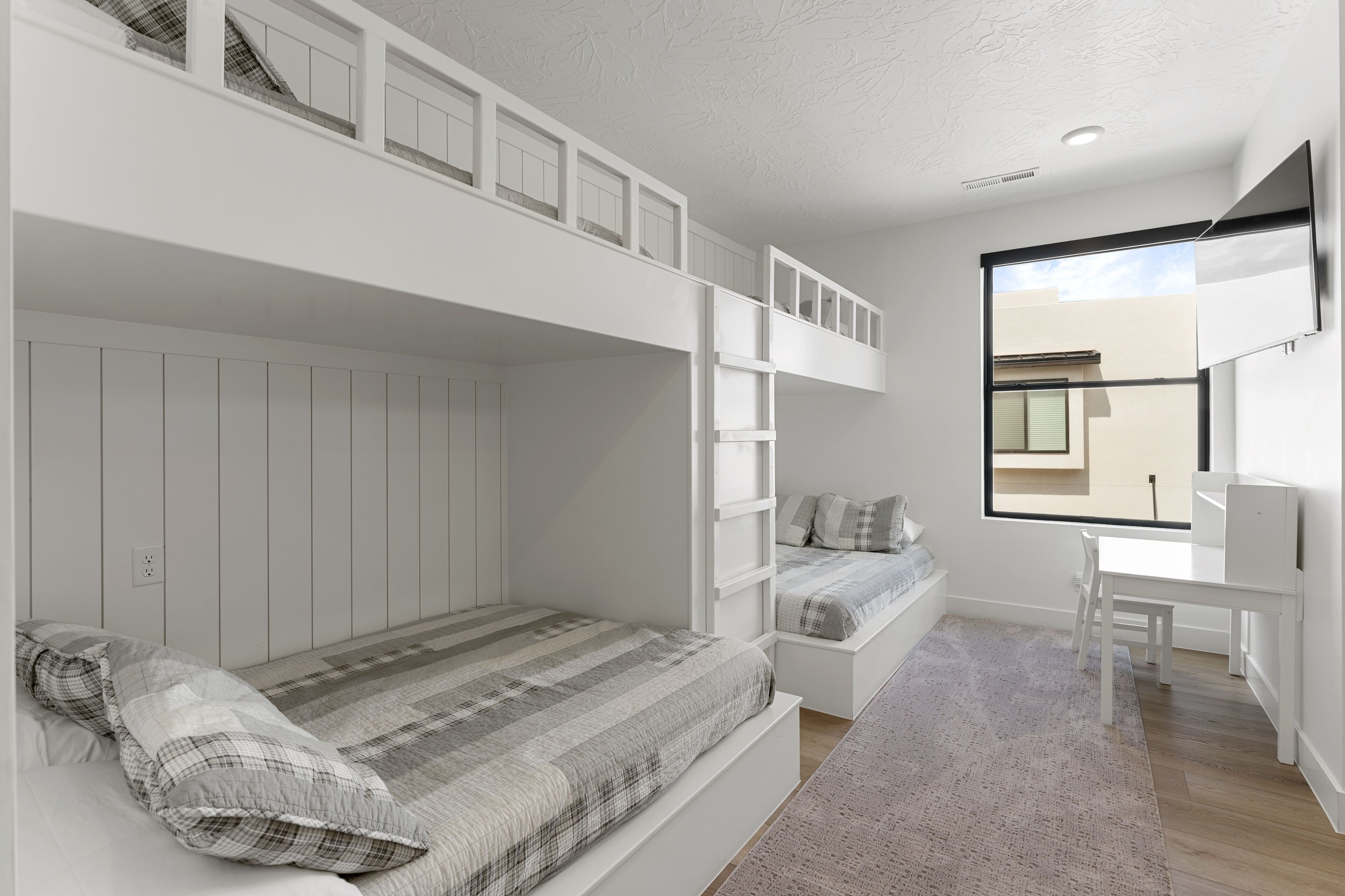 Une chambre à coucher moderne et minimaliste, avec des lits superposés, un bureau et une grande fenêtre donnant sur l’extérieur.