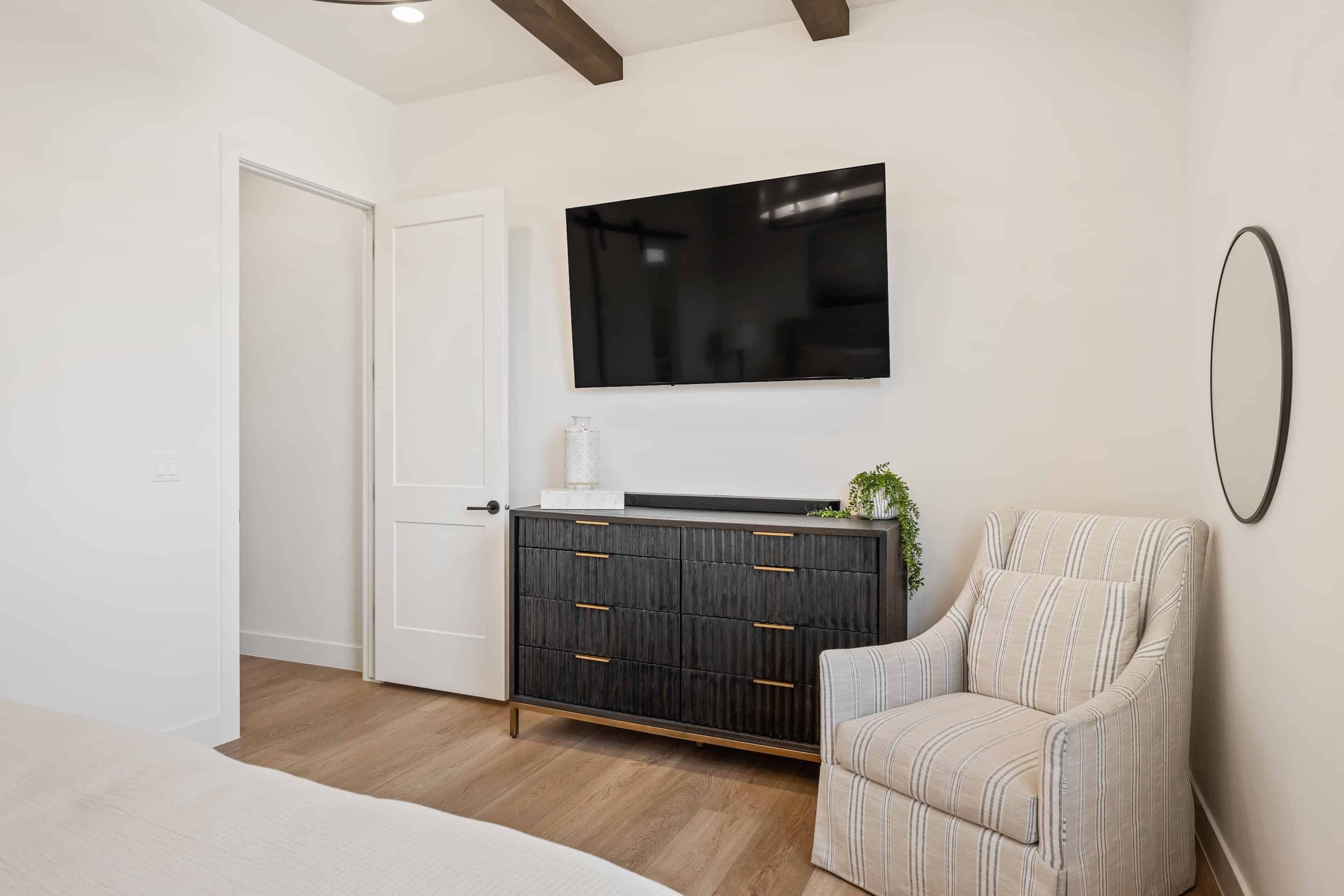 Un dormitorio moderno con un aparador de madera oscura, un televisor de pantalla plana, un sillón a rayas y una puerta blanca.