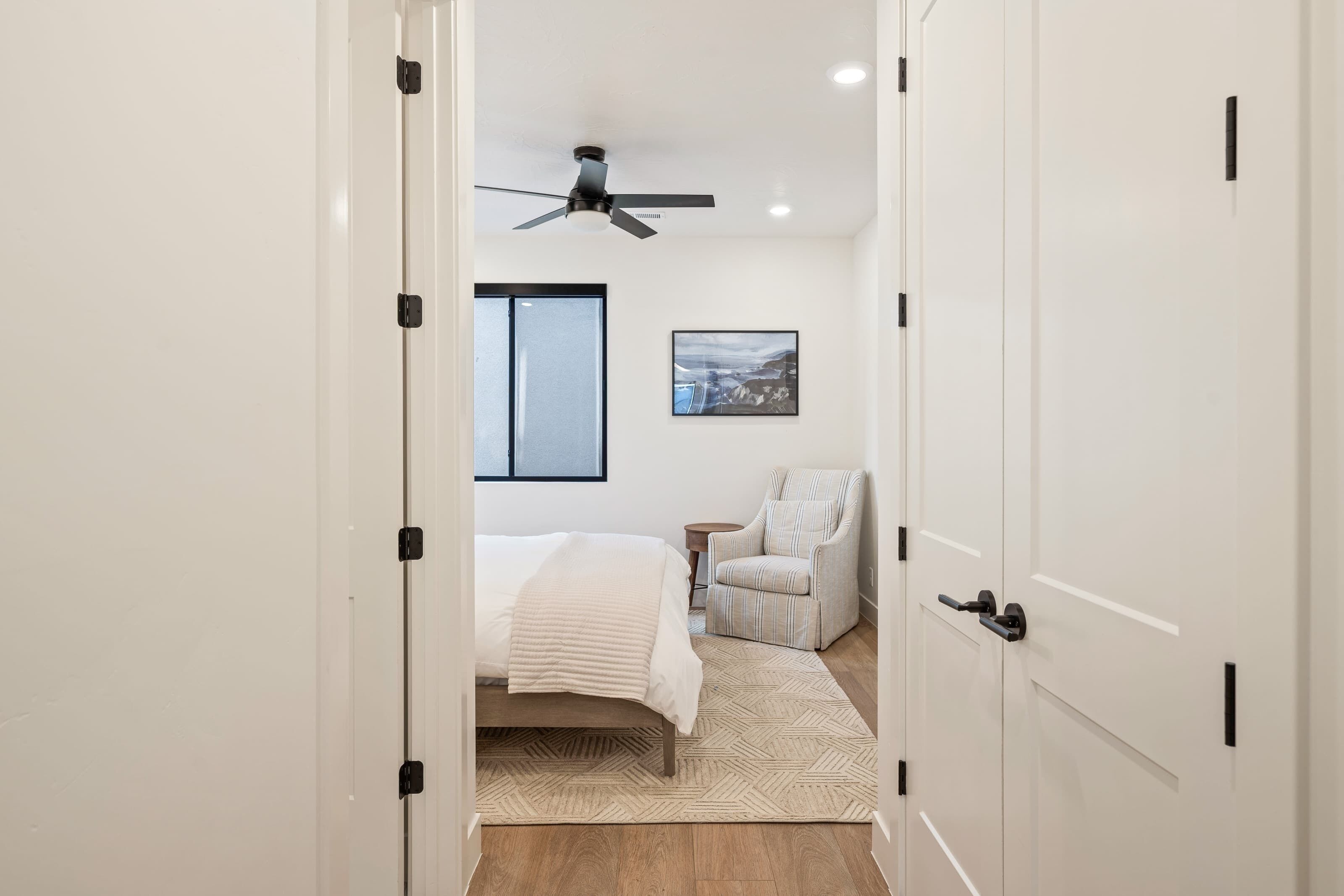A bedroom with a bed, a chair, a ceiling fan, and a window.