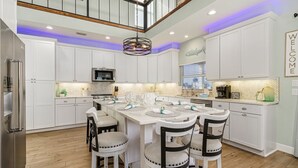 A spacious kitchen with white cabinetry, a central island with chairs, and a hanging light fixture.