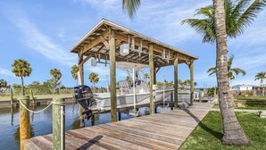 A wooden dock with a covered boat storage area, a motorboat, and palm trees in the background.