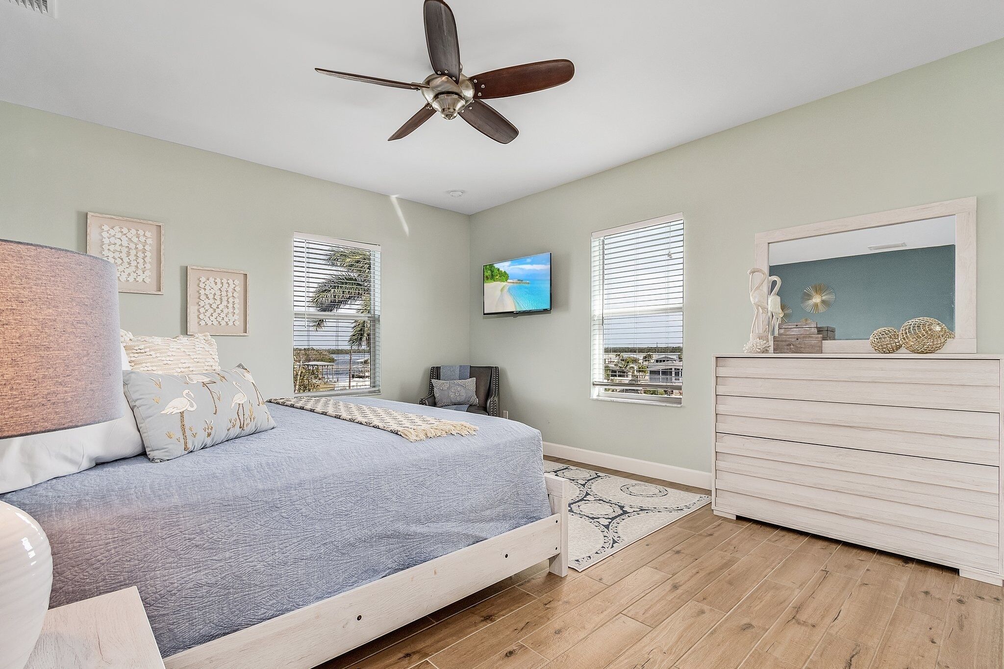 A bedroom with a bed, a dresser, a ceiling fan, and a TV on the wall.