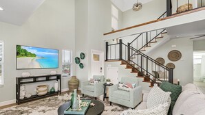 A spacious living room with a large flat-screen TV, a staircase, and a cozy seating area with a coffee table.