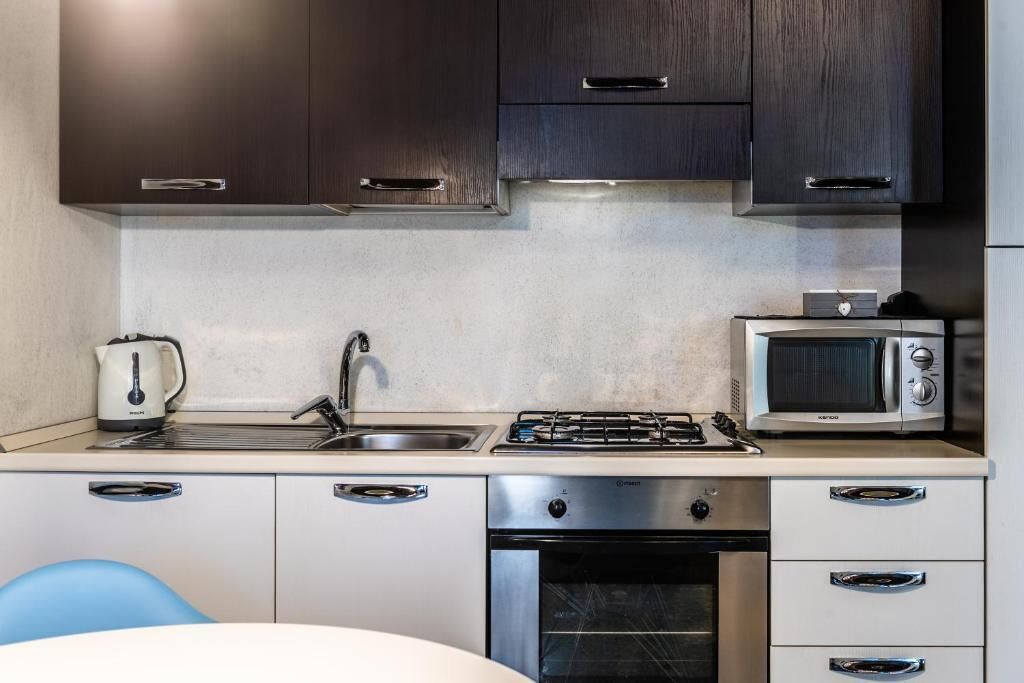 A modern kitchen with dark cabinets, stainless steel appliances, and a blue chair.
