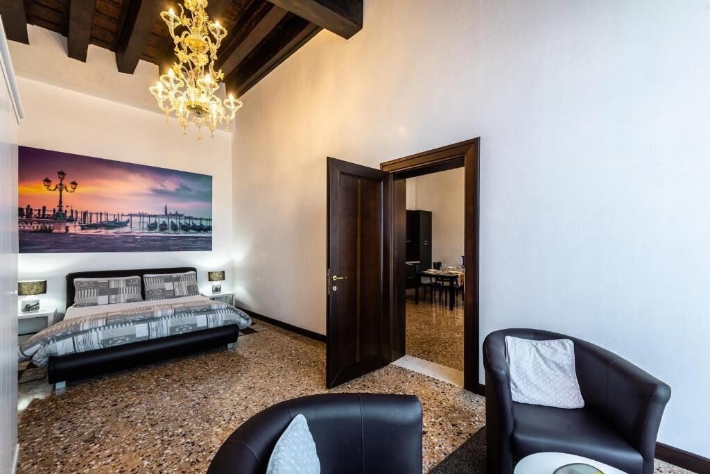 A bedroom with a bed, a painting, a chandelier, a door, and a chair.