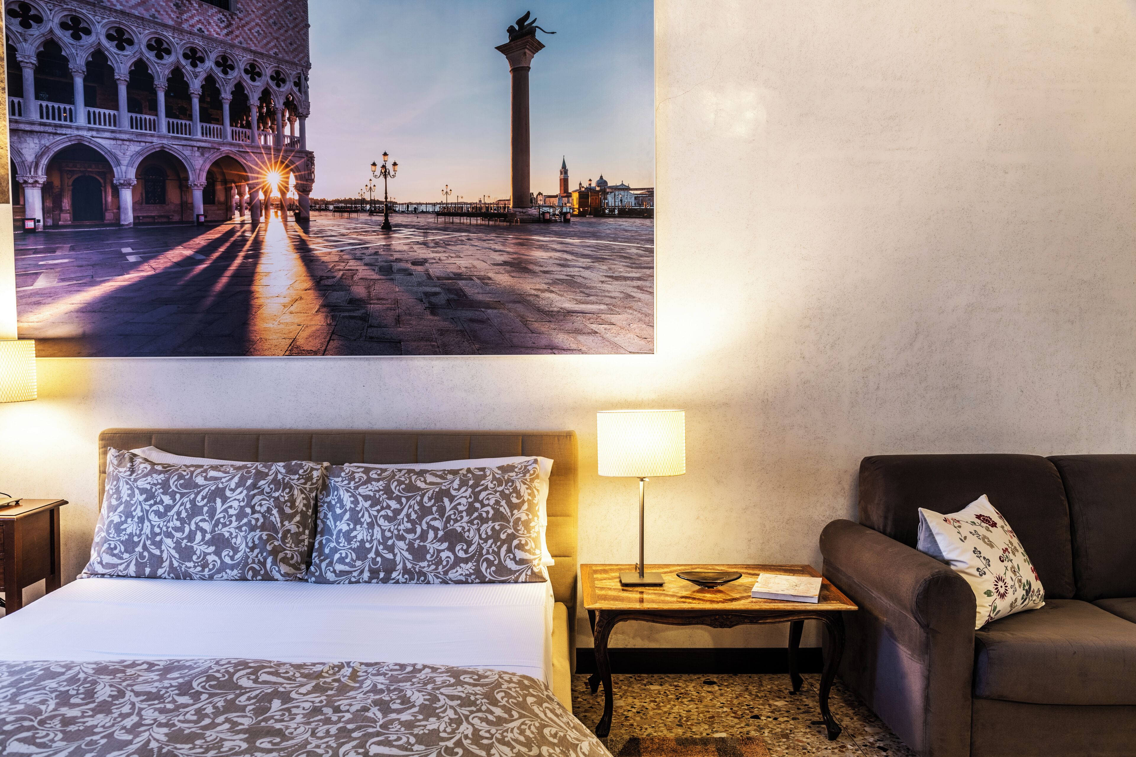 A hotel room with a bed, a nightstand, a lamp, and a sofa.